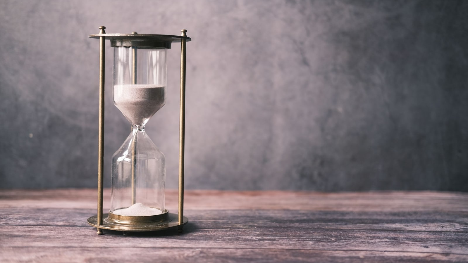 Metal framed hourglass with most of the sand in the upper bulb on a wooden table