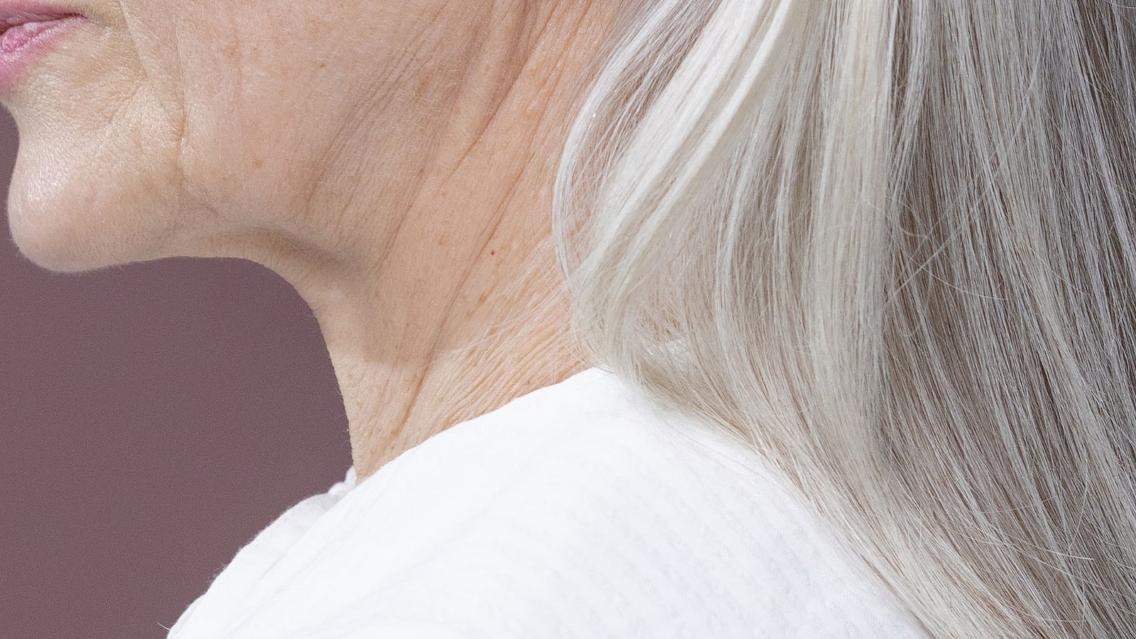 Side view of an older woman's jawline and neck against a mauve studio backdrop